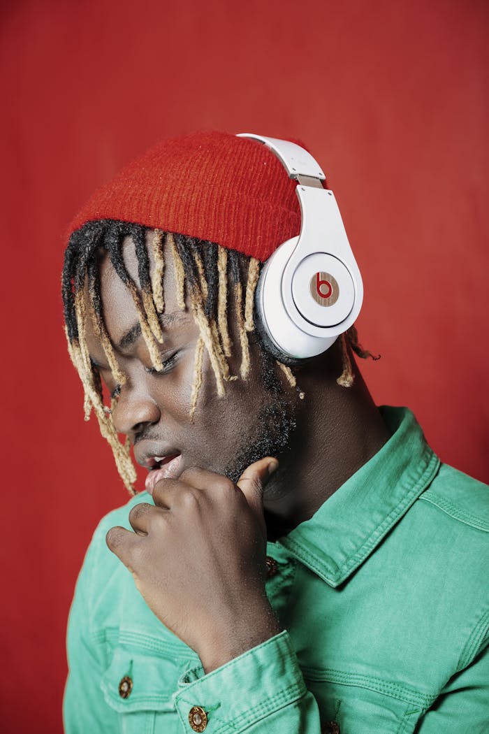 Fashionable man in headphones and green jacket against a red backdrop.