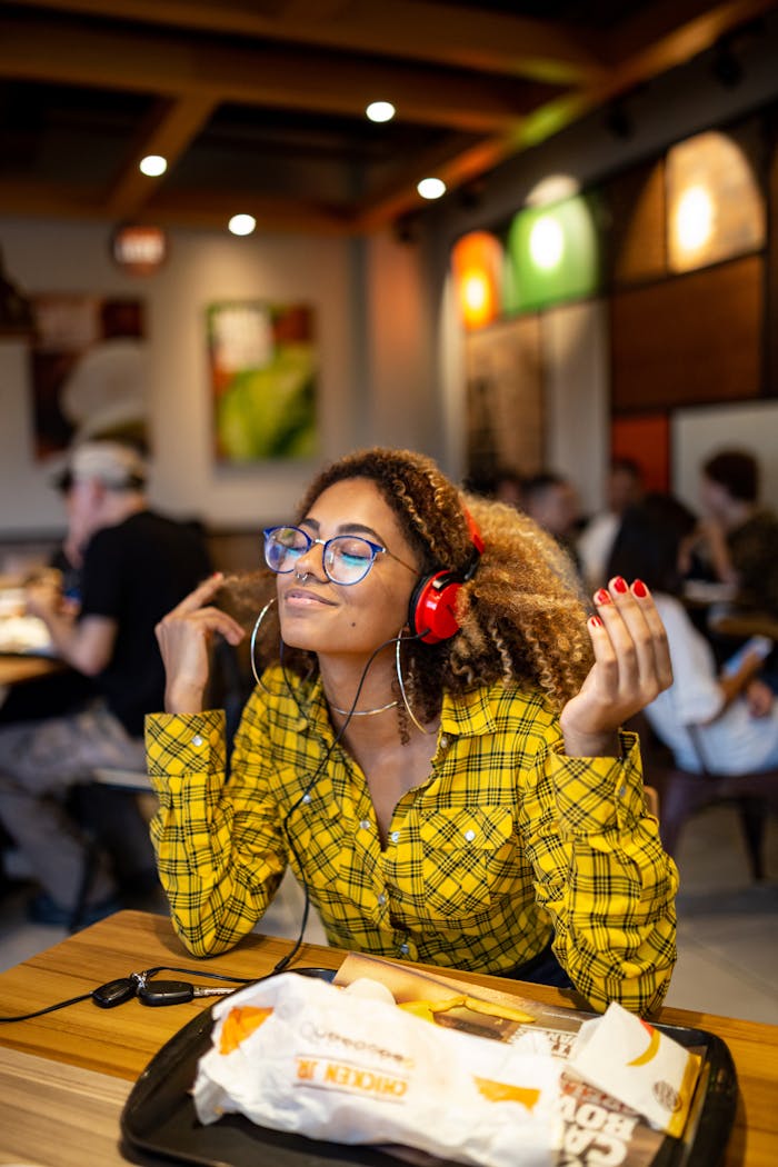 A stylish young woman with headphones enjoying music at an indoor cafe.