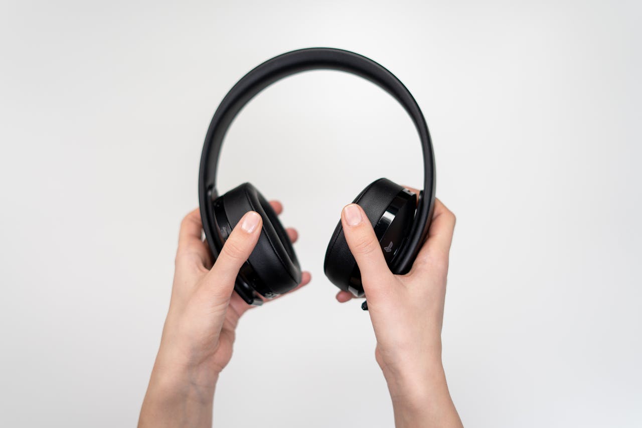 Close-up of hands holding black wireless headphones against a white background.